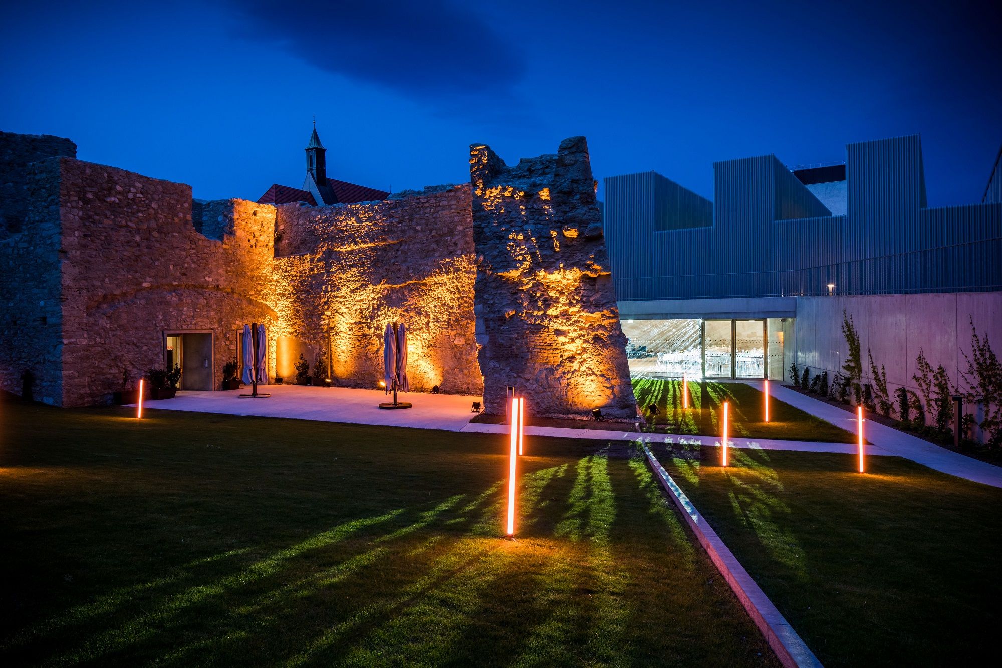 Beleuchtete Ruinen und moderne Architektur bei Nacht.