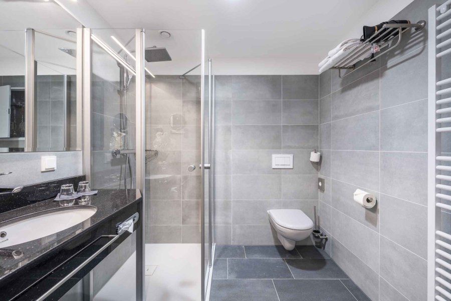 Modernes Badezimmer mit grauen Fliesen, Dusche, Waschbecken und WC.