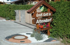Willkommensschild mit der Aufschrift 'Grüß Gott in Altendorf' vor einer Hecke.
