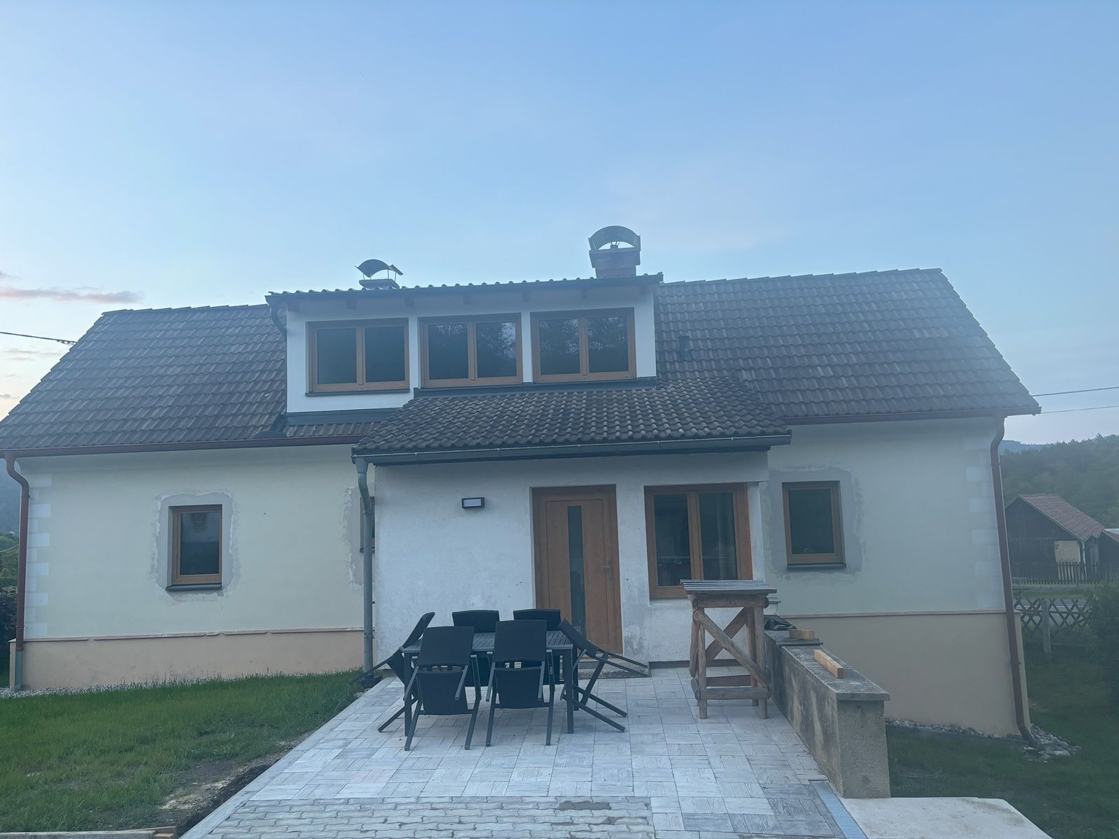 Ein zweistöckiges Ferienhaus mit Dachschindeln und Terrasse, umgeben von Rasen und ländlicher Umgebung.