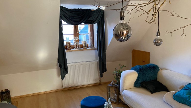 Cozy living room with sofa, wooden floor, windows with curtains, decorative candles and hanging lamps.