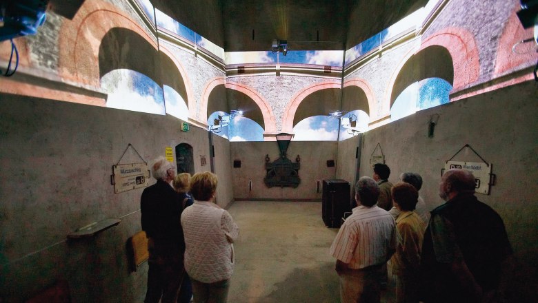 Visitors view a projection of a viaduct in a room with concrete walls.