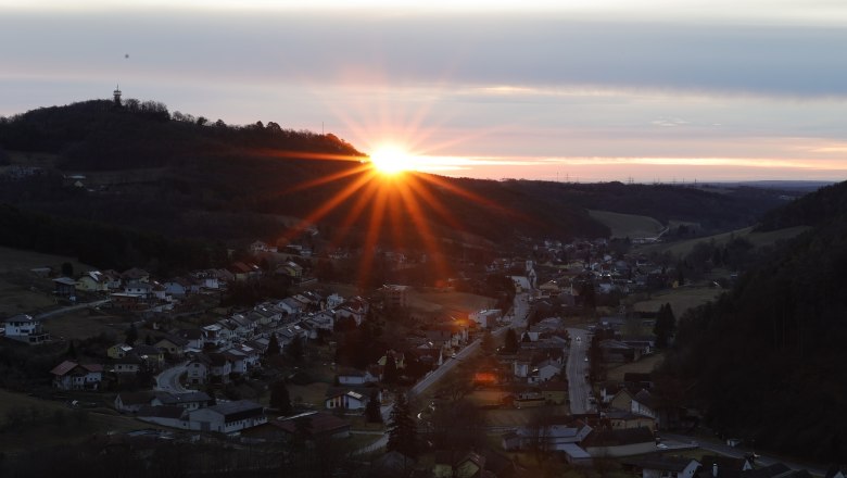 Sonnenaufgang hinter einem Hügel mit einem Dorf im Vordergrund.