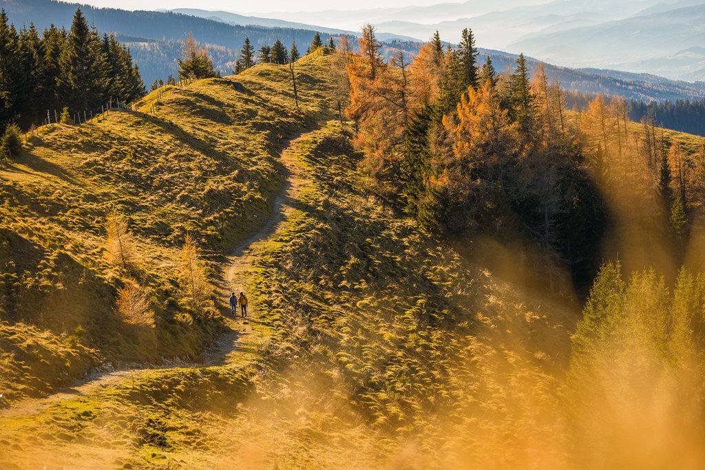 Zwei Wanderer auf einem herbstlichen Bergpfad mit bunten Bäumen.