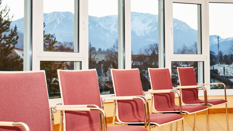 Seminar room with red chairs and mountain views through large windows.