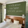 A double room with two beds, a green wall with a slogan, curtains and a shower with a glass wall.