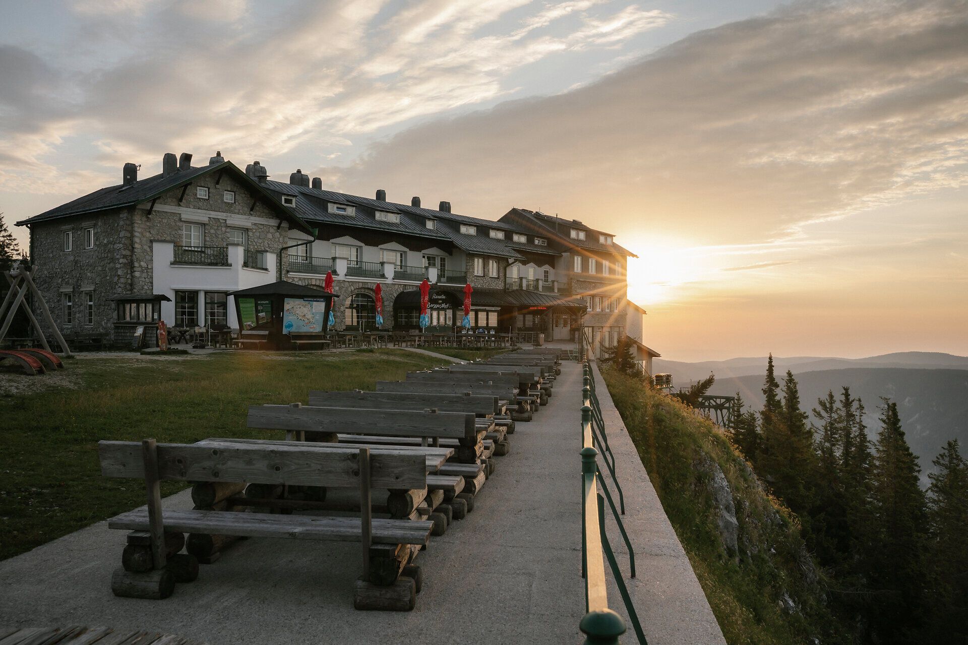 Sonnenuntergang über dem Raxalm-Berggasthof mit Sitzbänken auf der Terrasse