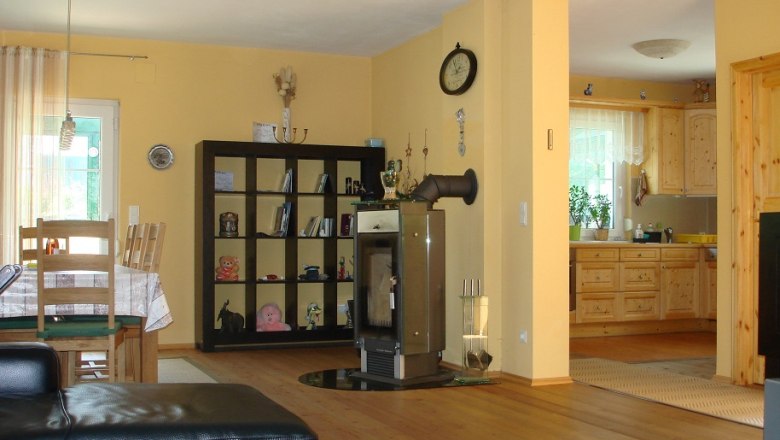 Wohnküche mit Holzmöbeln, Esstisch, Regal, Kamin und offener Küche.