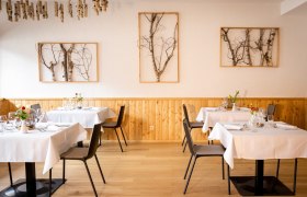 Elegantes Restaurant mit Holzwänden, weißen Tischdecken und Birkenkunst an den Wänden.