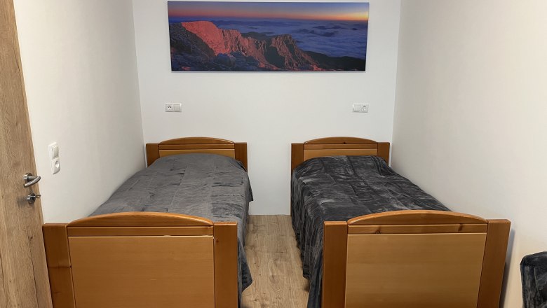 A simply furnished room with two single beds and a landscape painting on the wall.