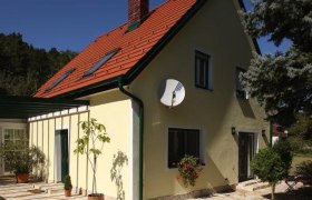 Gelbes Haus mit rotem Dach und Satellitenschüssel, umgeben von Bäumen.