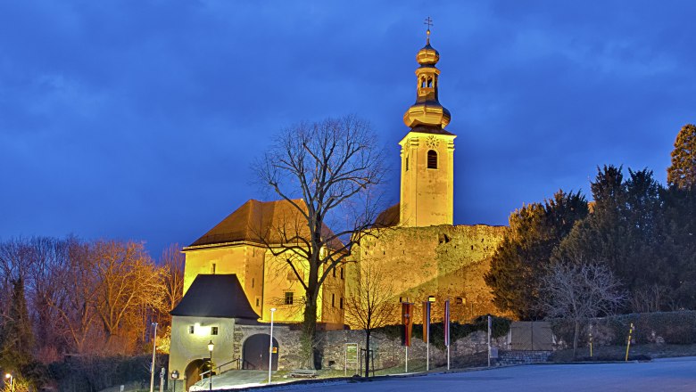 Beleuchtetes Schloss Gloggnitz bei Dämmerung mit blauem Himmel.
