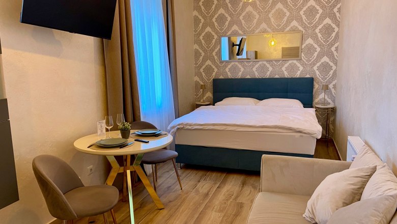 Ein gem&uuml;tliches Hotelzimmer mit Doppelbett, kleinem Esstisch und Sofa.