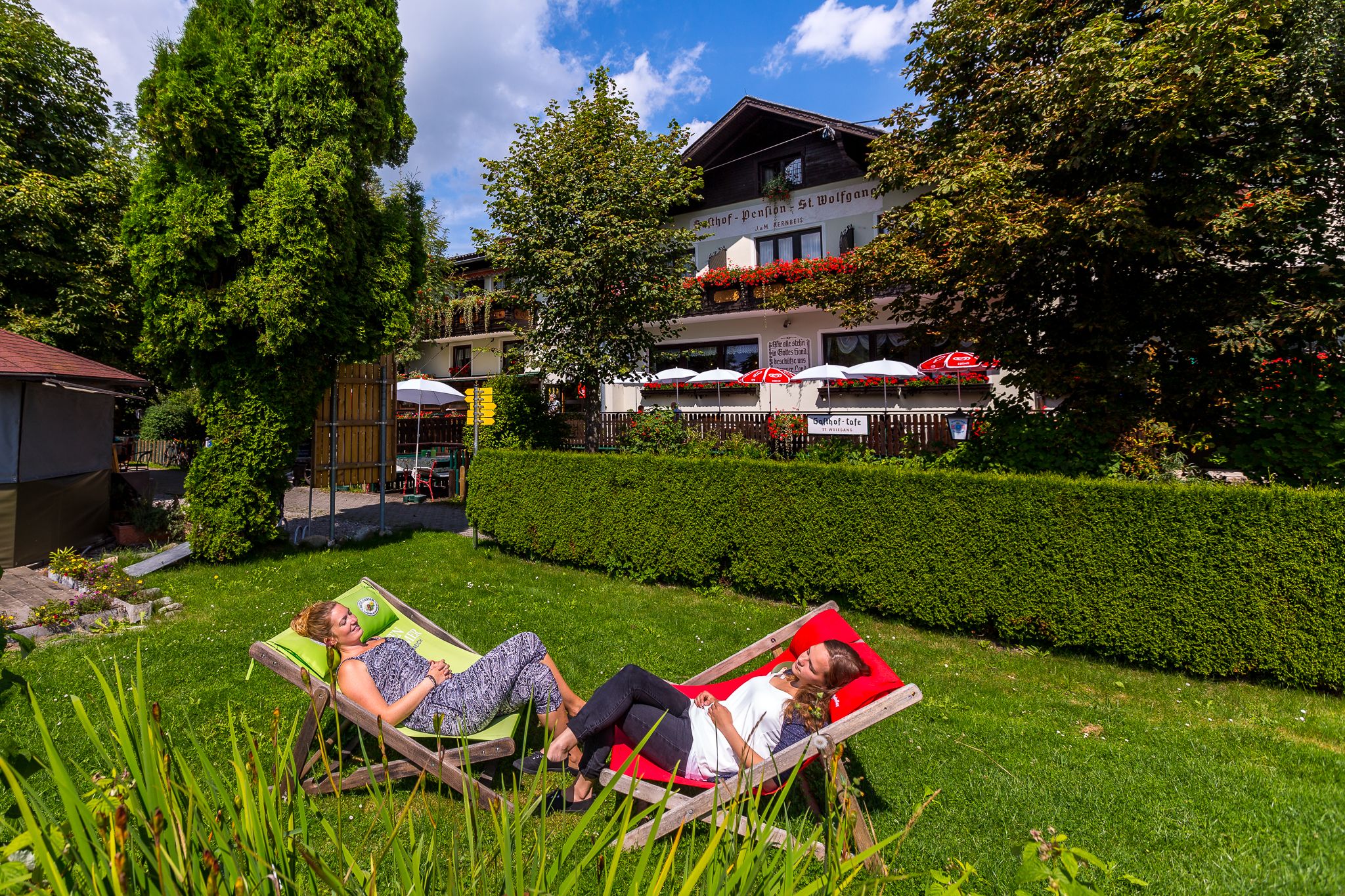 Zwei Frauen entspannen in Liegestühlen im Garten eines Gasthofs.